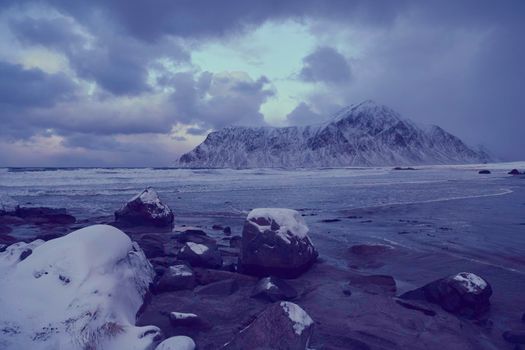 scandinavian coast at winter with mountains covered with snow in background and bad cloudy weather