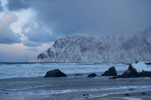 scandinavian coast at winter with mountains covered with snow in background and bad cloudy weather