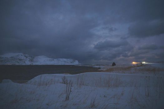 scandinavian coast at winter with mountains covered with snow in background and bad cloudy weather