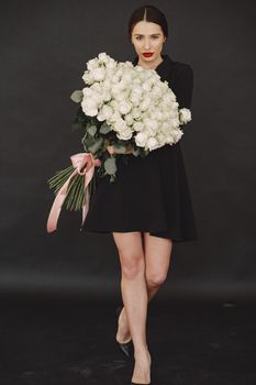 Beautiful girl in a studio. Stylish girl on a black background. Lady with bouquete of roses.
