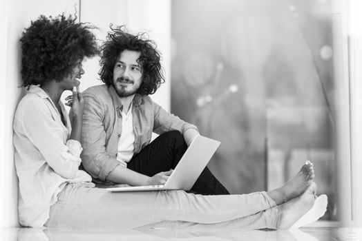 Young beautiful multiethnic couple using a laptop and doing shopping online while sitting on the floor