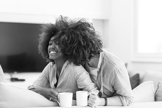 young multiethnic couple sitting on sofa at home drinking coffe, talking, smiling.