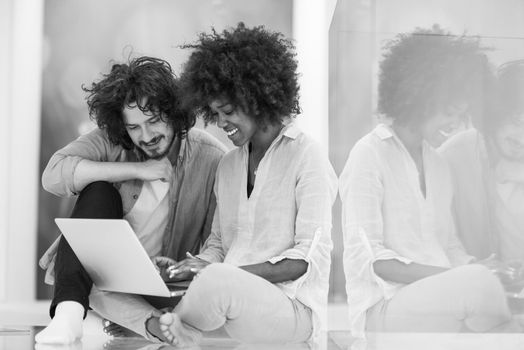 Young beautiful multiethnic couple using a laptop and doing shopping online while sitting on the floor