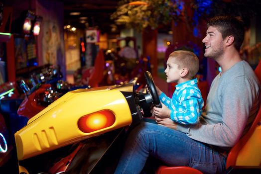 happy father and son playing driving wheel video game in playground theme park