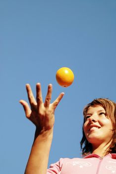 beautiful young woman throwing fresh orange in to air