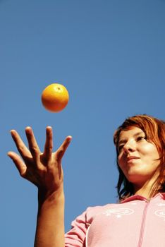 beautiful young woman throwing fresh orange in to air