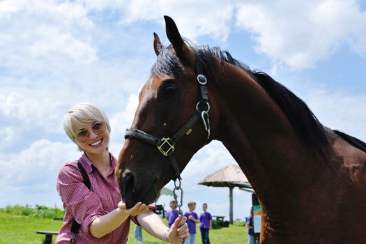 happy woman in sunglasses sitting on horse farm animal outdoors with blue sky in background