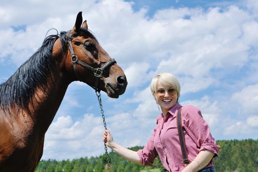 happy woman in sunglasses sitting on horse farm animal outdoors with blue sky in background