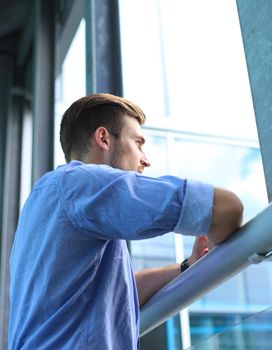 Young man standing near window in his office while thinking about his goals
