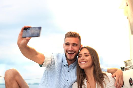 Happy couple taking a selfie after engagement proposal at sailing boat, relaxing on a yacht at the sea.