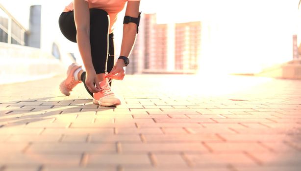 Young fitness attractive sporty girl runner ties up the shoelaces on her sports shoes getting ready to run