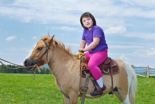 happy child ride farm animal brown pony with blue sky in background and beautiful nature