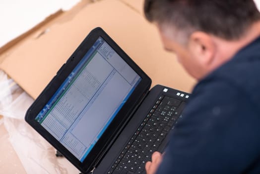 man checking business workflow using laptop computer while lying on floor with cardboard box placed below him during renovation of the apartment
