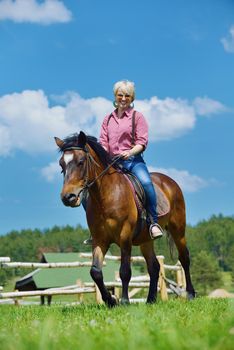 happy woman in sunglasses sitting on horse farm animal outdoors with blue sky in background