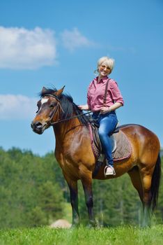 happy woman in sunglasses sitting on horse farm animal outdoors with blue sky in background