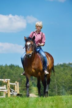 happy woman in sunglasses sitting on horse farm animal outdoors with blue sky in background