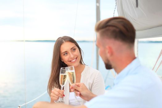 Smiling young couple with champagne and looking at each other while sitting on the board of yacht.