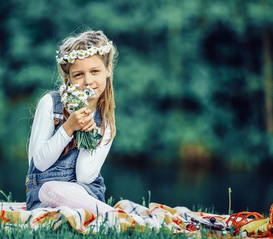 cute little girl in a wreath and a bouquet of wildflowers on a picnic in the woods on a Sunny day