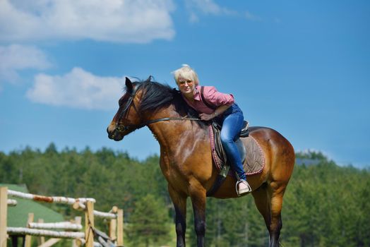 happy woman in sunglasses sitting on horse farm animal outdoors with blue sky in background