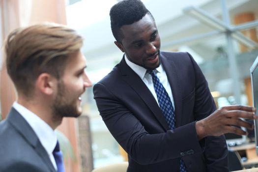 Two multinational young businessmen discussing business at meeting in office.