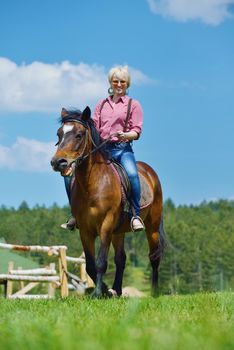 happy woman in sunglasses sitting on horse farm animal outdoors with blue sky in background