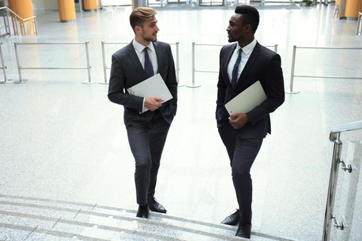 Two multinational young businessmen talking while stairs in modern office building.