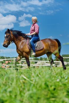 happy woman in sunglasses sitting on horse farm animal outdoors with blue sky in background