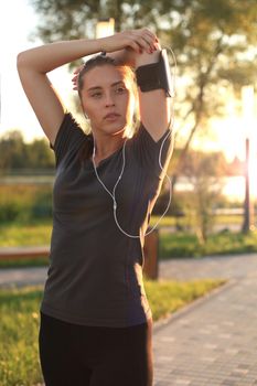 Young girl warming up outdoors, stretching triceps and neck muscles before workout