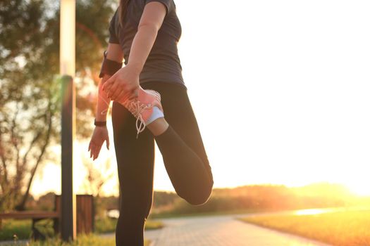 Young attractive sporty fitness woman runner warming up before run at sunset or sunrise on city
