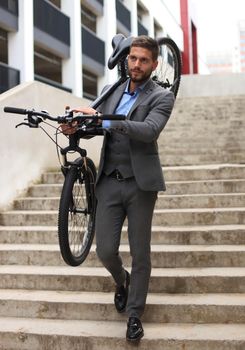 Confident young businessman carrying his bicycle while walking outdoors.