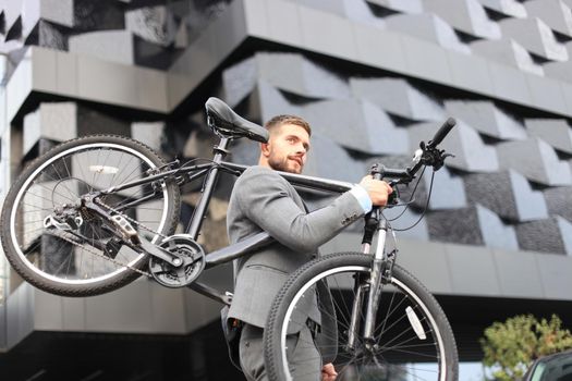 Confident young businessman carrying his bicycle while walking outdoors.
