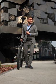 Confident young businessman walking with bicycle on the street in town.