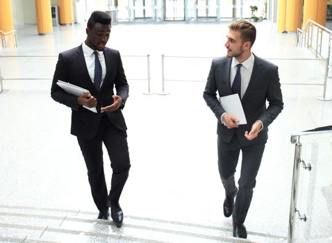 Two multinational young businessmen talking while stairs in modern office building.