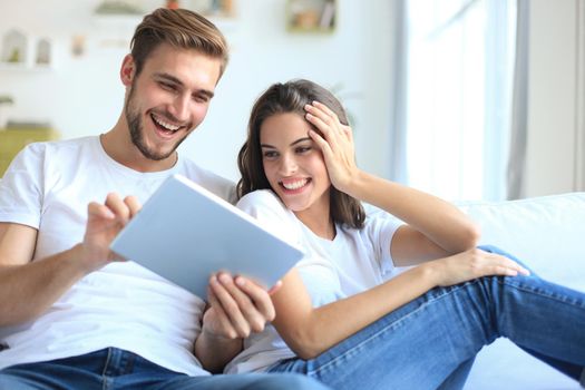 Young couple watching media content online in a tablet sitting on a sofa in the living room.