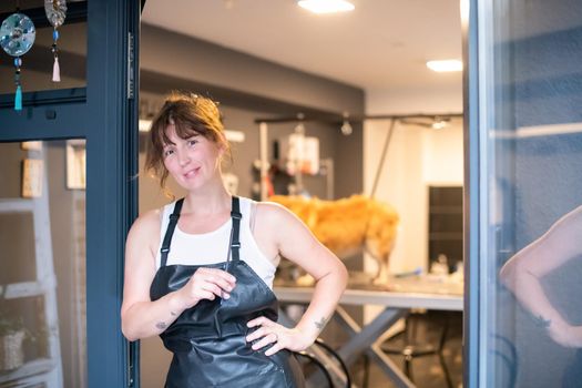 portrait of professional pet hairdresser hipster woman with tattoos while standing at the door of her beauty salon for animals