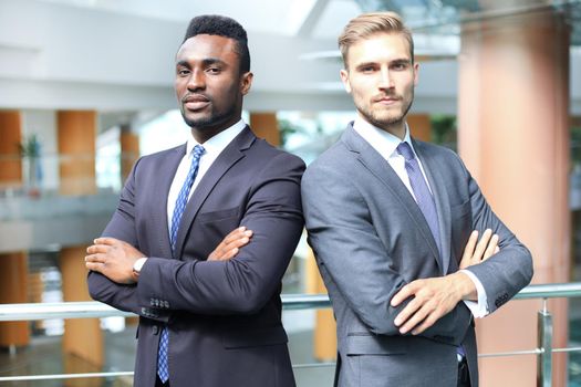 African american and caucasian business partners standing back to back together and looking in camera, in office.