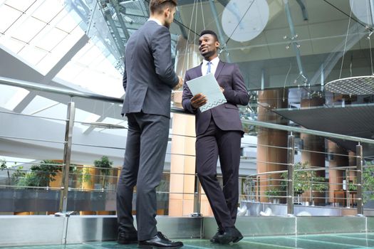 Two multinational young businessmen discussing business at meeting in office.