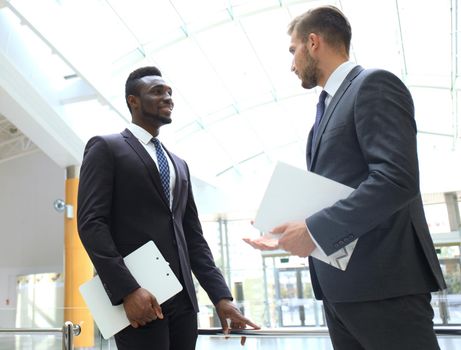 Two multinational young businessmen discussing business at meeting in office.