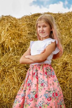 Blonde girl stands near a large stack of straw on a summer day