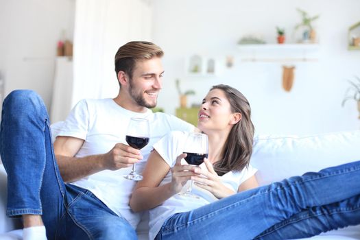 Young loving couple drinking a glass of red wine in their living room.