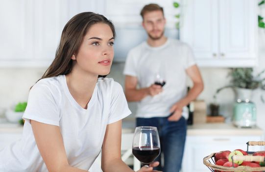 Pretty young woman drinking some wine at home in kitchen.