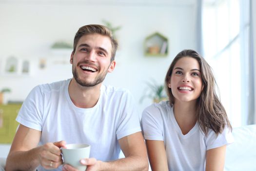 Young loving couple on sofa at home watching tv and laughing.