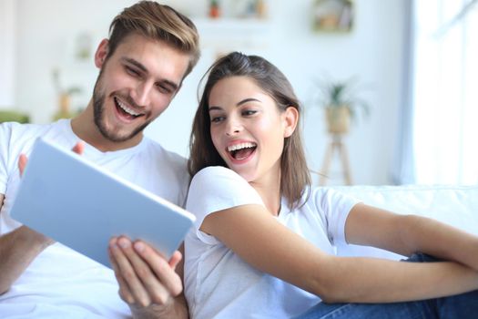 Young couple watching media content online in a tablet sitting on a sofa in the living room.