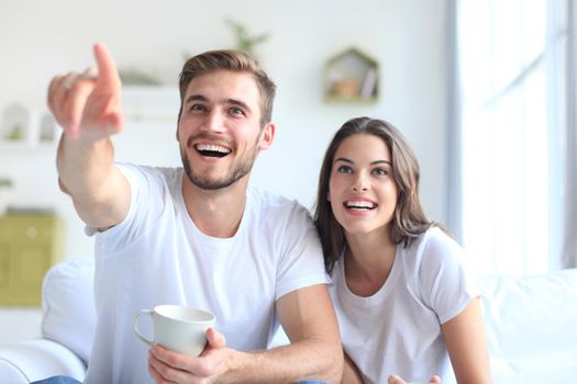 Young loving couple on sofa at home watching tv and laughing.