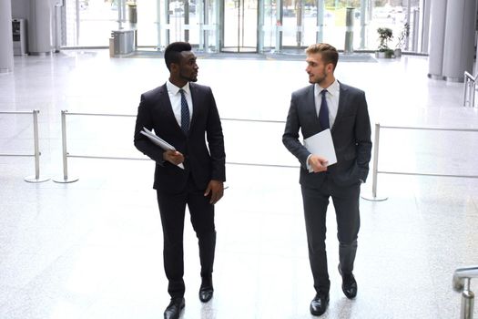 Two multinational young businessmen talking while stairs in modern office building.