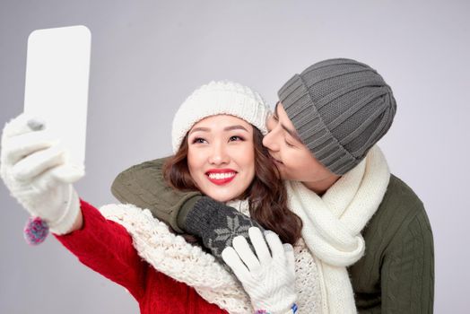 Happy couple in their winter clothes taking picture with smartphone