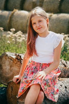 Blonde girl with long flowing hair sitting on a log in a pink dress