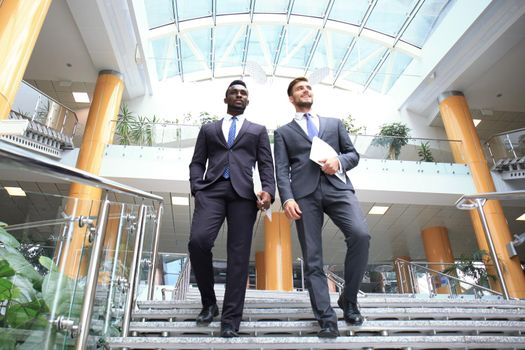 Two multinational young businessmen talking while stairs in modern office building.