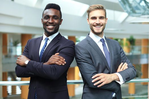 African american and caucasian business partners standing back to back together and looking in camera, in office.