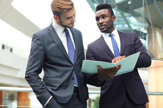 Two multinational young businessmen discussing business at meeting in office.